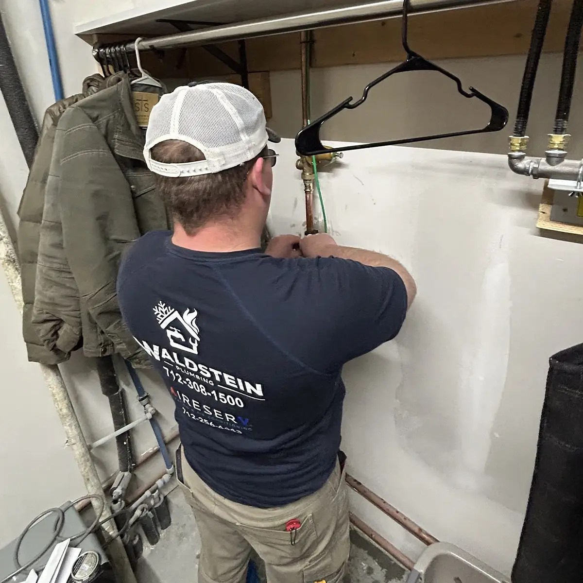 Man facing a wall and working on the piping against the wall.