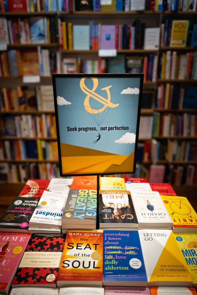 A display in a bookstore featuring a sign that reads 'Seek progress, not perfection' above a table filled with various books.