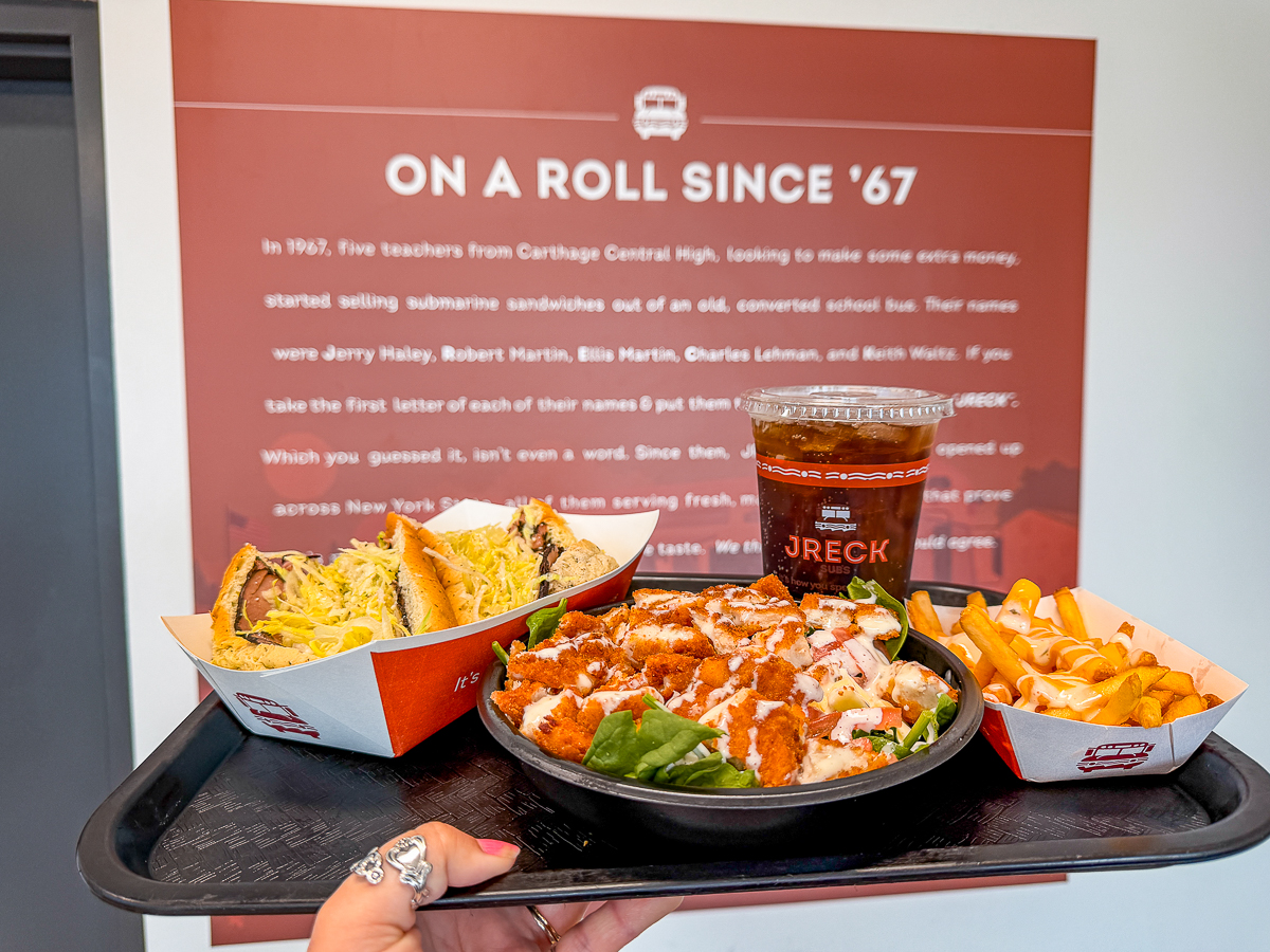 A tray of food at JRECK Subs in front of a sign documenting the history of the company