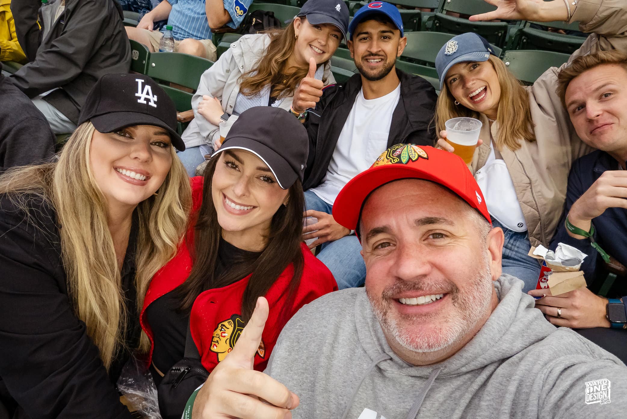 Group of excited baseball fans at a stadium, smiling and taking selfies, celebrating a special event during a game.