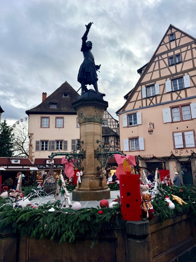 Fountain statue surrounded by Christmas decorations and half-timbered houses in Colmar