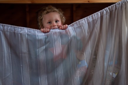 Warm Glow Photo T-7 Young boy hiding behind curtain. Photographed at home by Anna Hindocha/Warm Glow Photo
