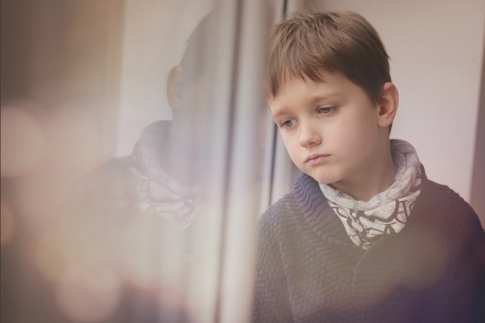 Sad thoughtful little boy looking through the window. Cabin Fever in Kids