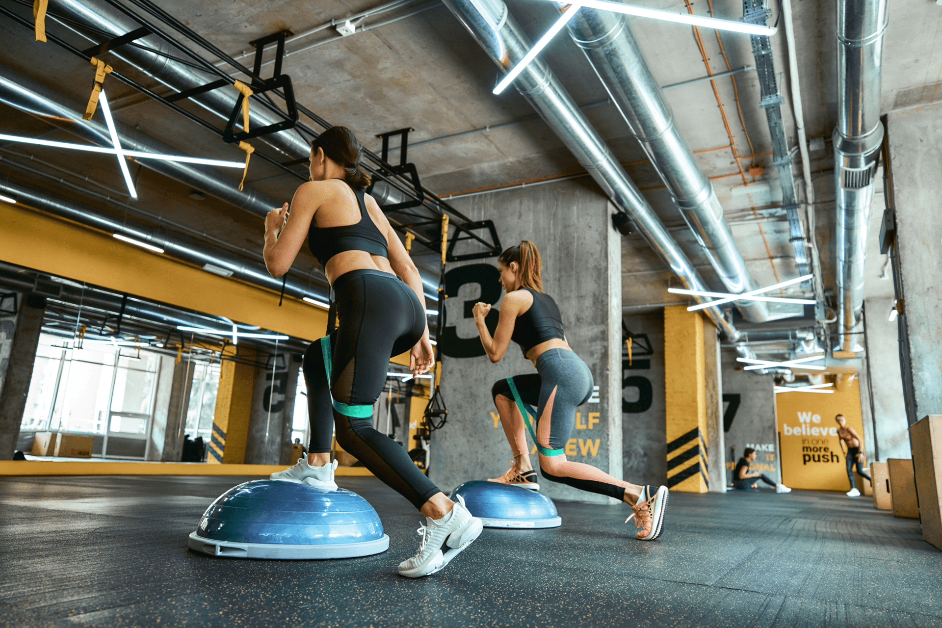 Personnes effectuant un exercice Dynamic Move sur un Bosu, combinant équilibre, mouvement et renforcement musculaire, en salle de sport.
