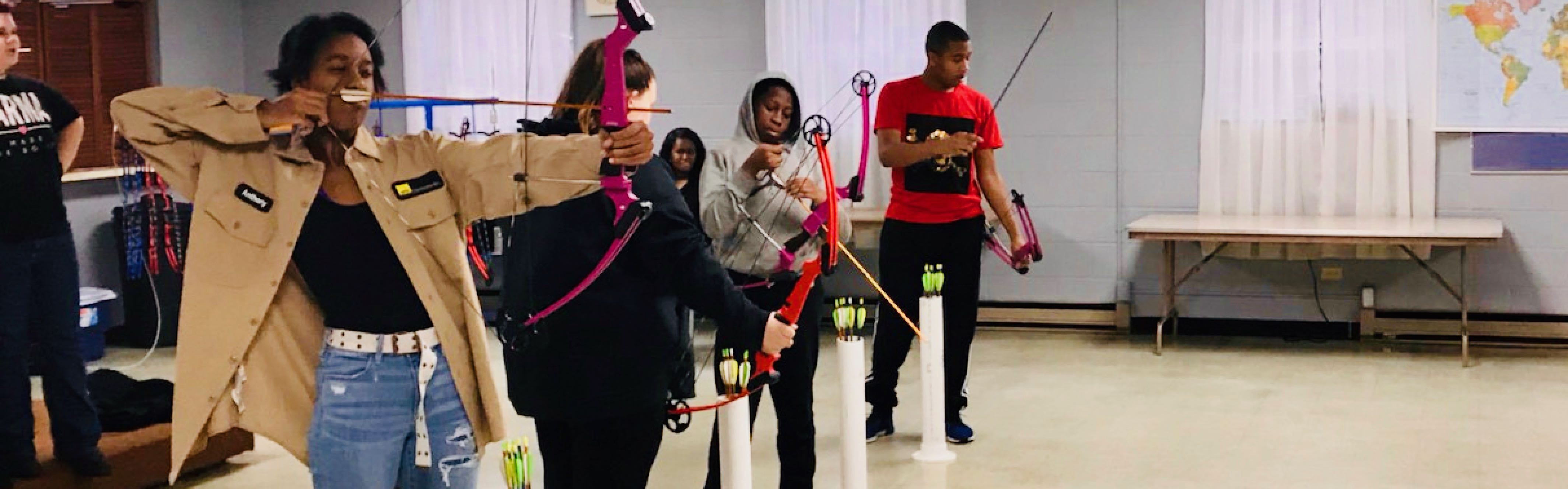 four teenagers holding archery bows and arrows