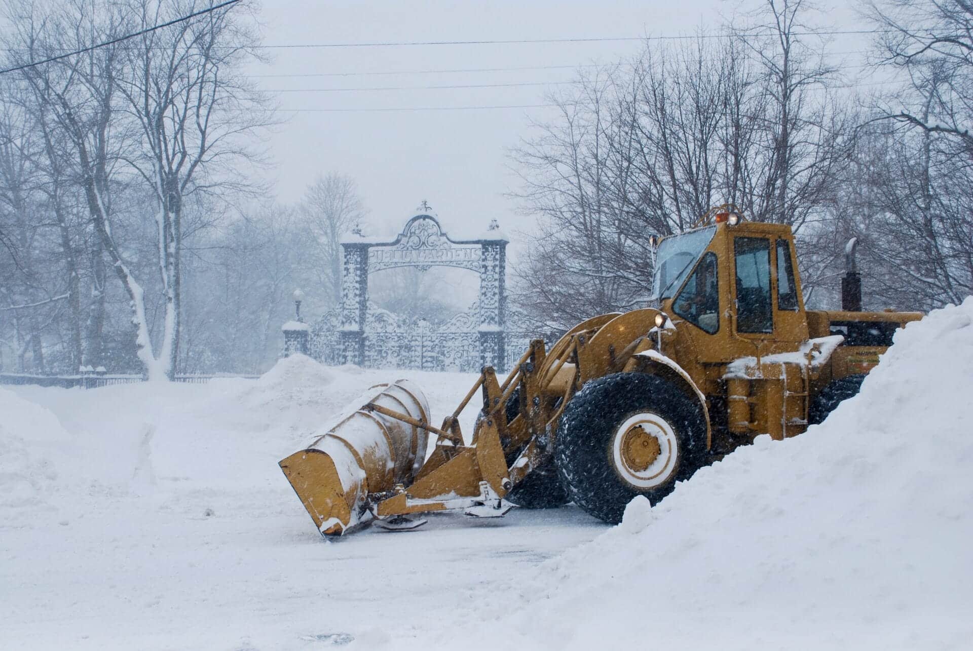 A yellow plow in front of the gates of the Public Gardens, surrounded by piles of snow.
