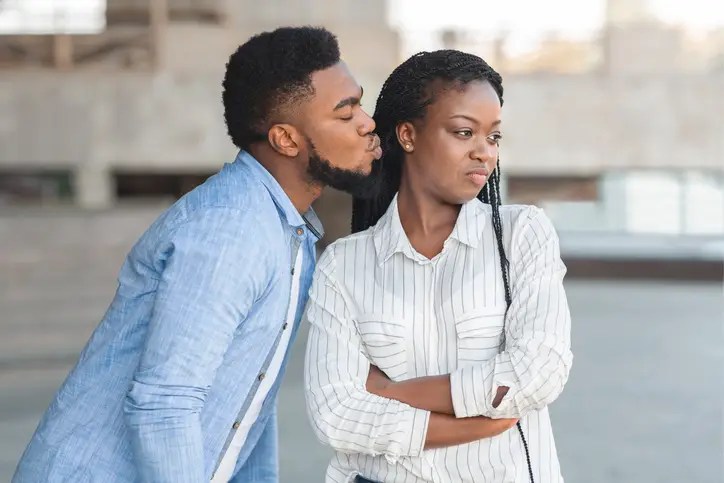 African American man leaning in to kiss displeased African American woman with braids.