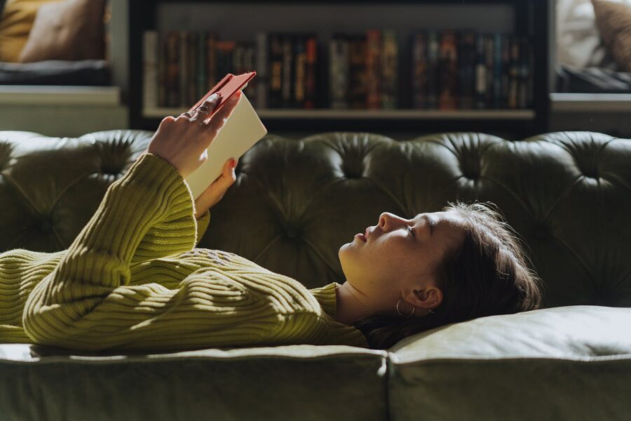 femme en chemise à manches longues jaune allongée entrain d lire un livre sur un canapé