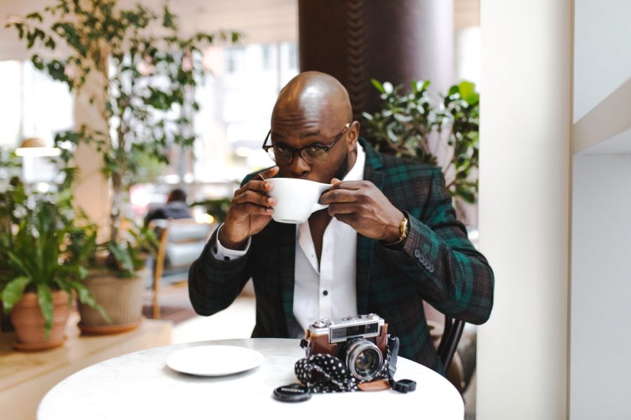 man sitting in front of round table while sipping from white ceramic mug: How to Make Money with Photography in South Africa (Guide)