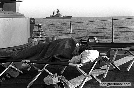 Fireman James Seward sleeps on the forecastle of the guided missile frigate SAMUEL B. ROBERTS (FFG-58). Some of the crew are sleeping on the deck because of hull damage sustained when the ship struck a mine on April 14, 1988. The guided missile cruiser USS JOUETT (CG-29) is in the background.
