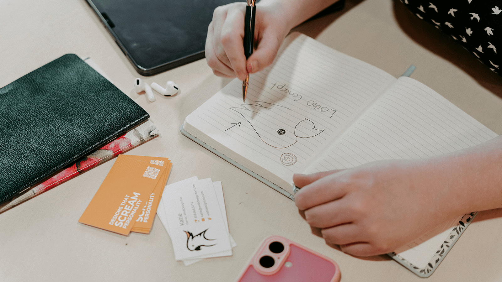 Woman drawing a preliminary sketch of a cockatoo logo, with business cards and notebooks around her