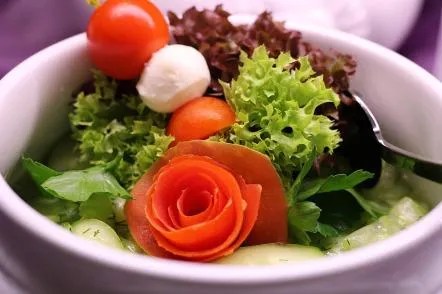 A delicious salad, featuring tomatoes curled into a rosette, in a white bowl.