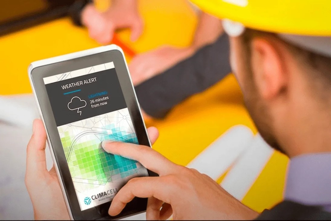 A worker standing and checking a weather app on a tablet, planning their day.
