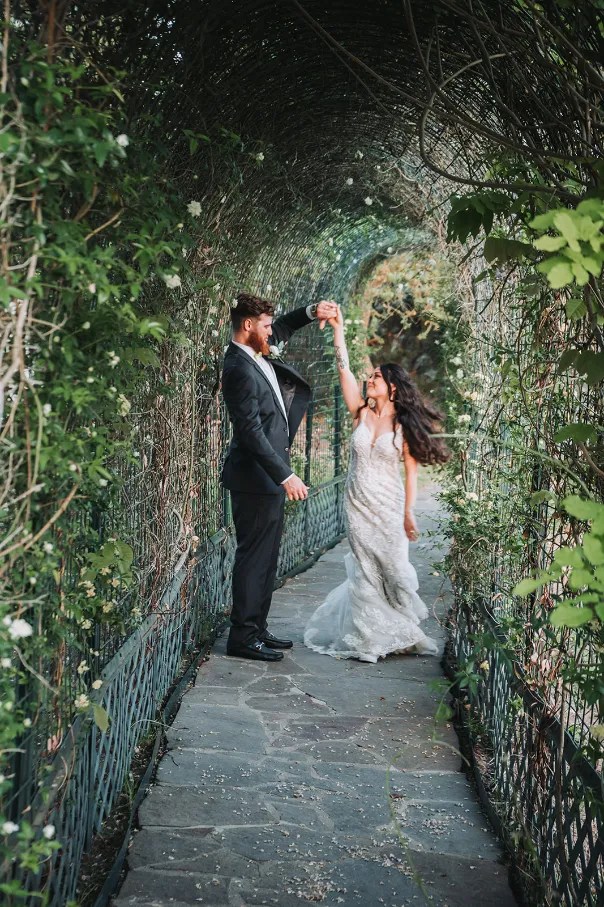 Taylor and Grayson Bride and groom dancing joyfully under a vine-covered archway during their wedding photo session, emphasizing romance and celebration.