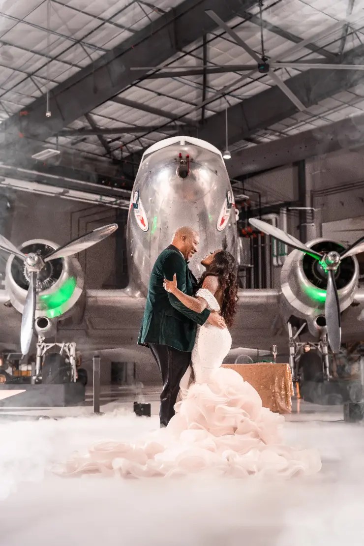 Flight Musuem A bride and groom share a romantic dance in front of a vintage airplane inside a hangar, surrounded by soft lighting and a misty atmosphere, highlighting affordable wedding photography and DJ services.