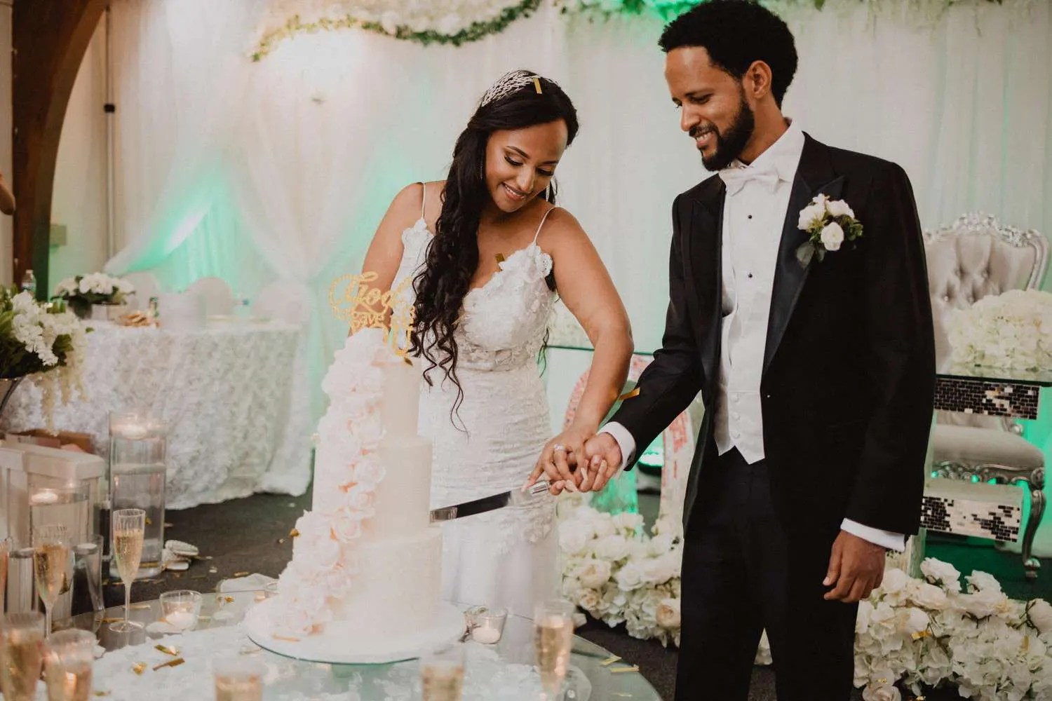 Couple cutting the cake under green uplighting at an Ethiopian/Eritrean wedding celebration, photographed by Weddings Unlimited