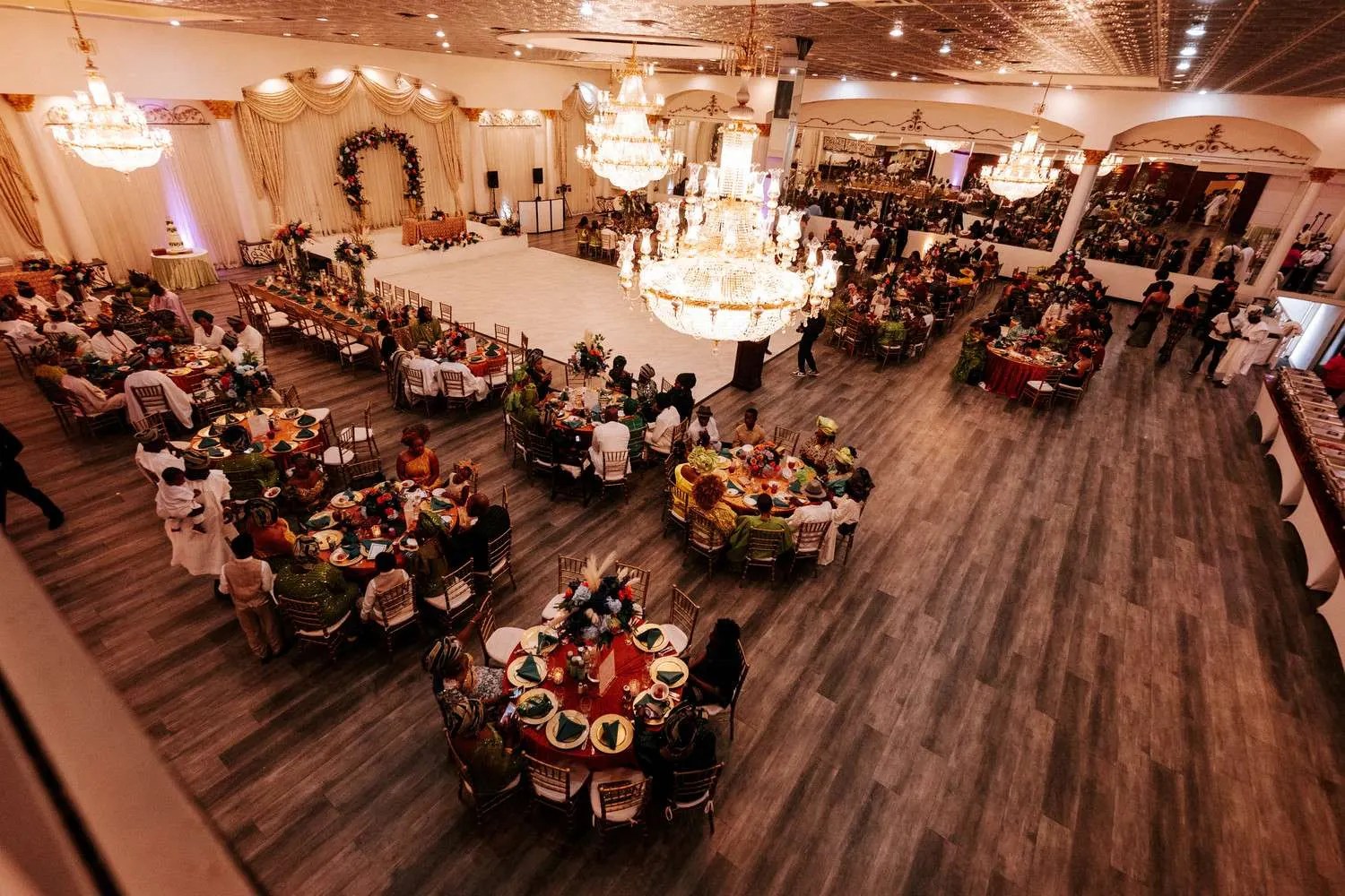 Wide view of a lively Nigerian wedding reception under a chandelier-lit ballroom, photographed by Weddings Unlimited