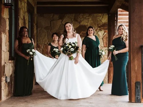 Bridesmaids in emerald gowns helping the bride with her train at The Springs Venue in Denton, Aubrey, TX