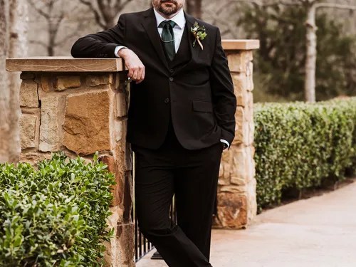 Groom leaning against the stone entrance at The Springs Venue in Denton, Aubrey, TX