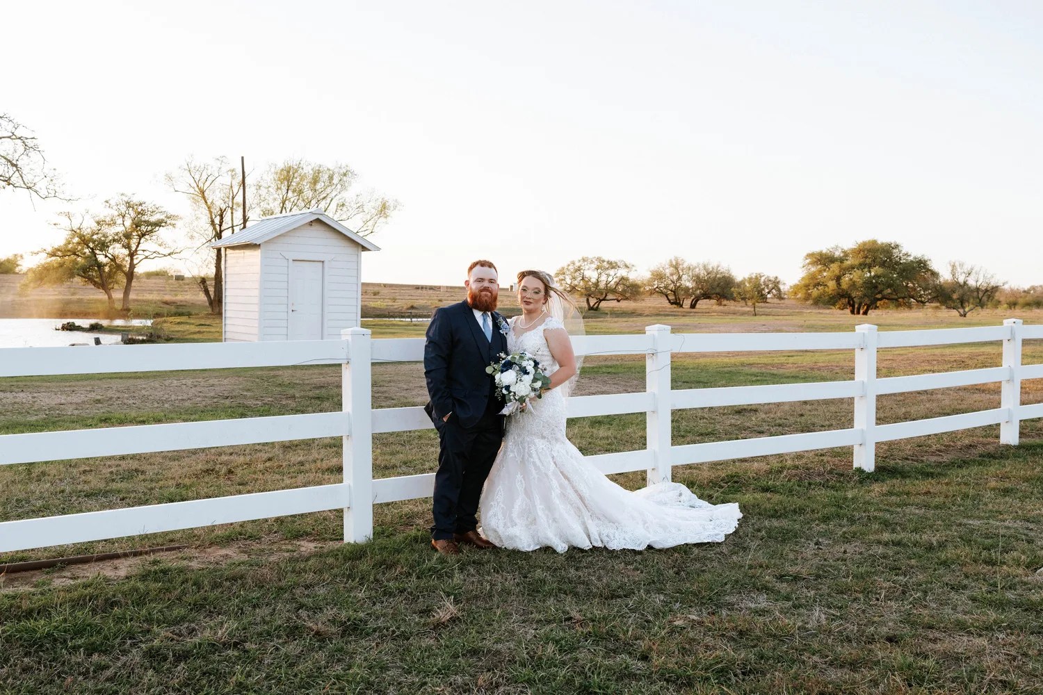 Couple by the white ranch fence at Teaghlach Meadows in Yorktown, Texas