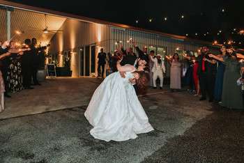 Bride and groom share first dance outdoors as guests form circle around them with sparklers at night