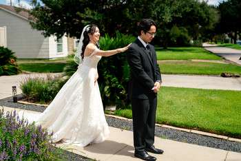 Bride in white ballgown and groom in black suit stand back-to-back on sidewalk for first look moment