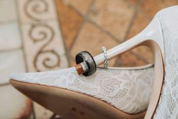 Wedding rings rest on white lace bridal heel with decorative tile in background
