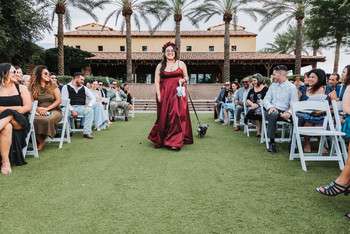 Bridesmaid in burgundy dress walks down outdoor ceremony aisle lined with white chairs and palm trees