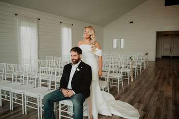 Bride and groom pose in white ceremony space with white chiavari chairs and shiplap walls at rustic venue