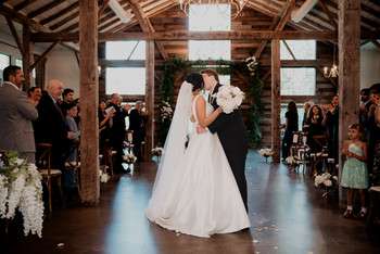 Bride and groom share first dance in rustic wooden barn venue with exposed beams and large windows
