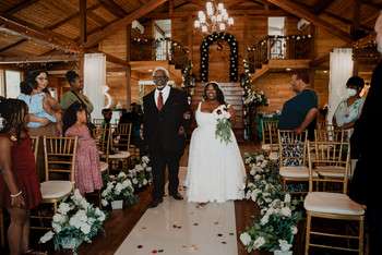 Bride and groom walking down aisle in rustic wood pavilion with chandelier and white floral arrangements
