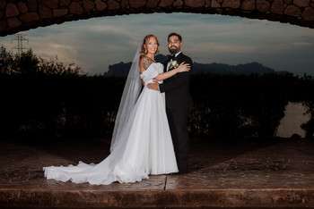 Bride and groom standing together under stone archway at dusk with mountains visible in background