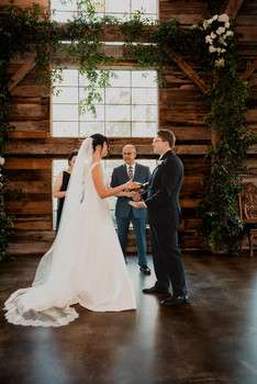 Bride and groom holding hands during indoor ceremony with officiant before white tile and wood backdrop