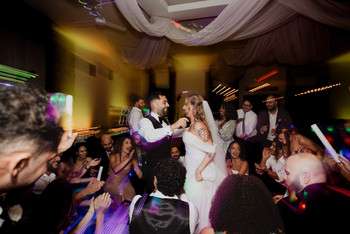 Bride and groom dancing on crowded reception dance floor with colorful uplighting and draped fabric ceiling