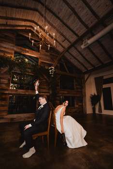 Bride and groom sitting on wooden bench in rustic barn venue with exposed beams and chandelier lighting