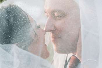 Bride and groom sharing an intimate moment under bride's veil with sunlight streaming through
