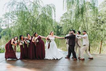 Wedding party in burgundy dresses and black suits celebrating under willow trees on outdoor patio
