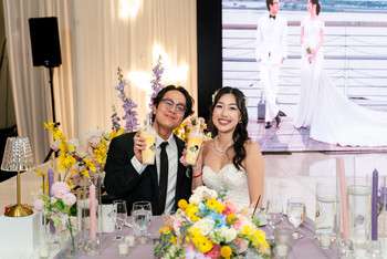 Bride and groom seated at sweetheart table with yellow and white floral arrangements and lit candles