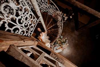 Overhead view of bride in white lace wedding dress walking up wooden staircase holding dried flower bouquet