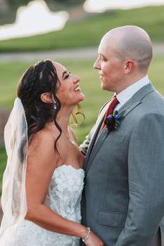 Bride in strapless white gown and groom in gray suit share an intimate moment on golf course