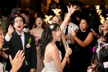 Bride in strapless wedding dress celebrates with guests holding sparklers on dance floor at evening reception