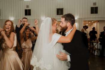 Bride and groom sharing first dance while wedding guests watch and take photos in rustic barn reception venue
