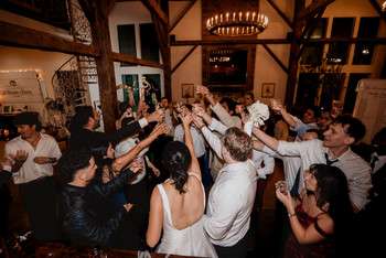 Wedding guests dancing and celebrating on dance floor under chandelier in rustic barn venue