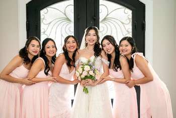 Bride in white gown with bouquet surrounded by five bridesmaids in matching light pink dresses
