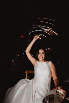 Bride in white wedding dress laughing with arm raised as light trails swirl above her on dance floor
