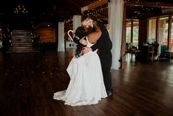 Bride and groom share first dance in rustic reception venue with wood floors and draped ceiling