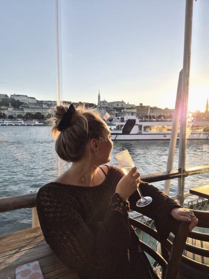 Cute girl looking out over Danube River from cruise boat with wine glass