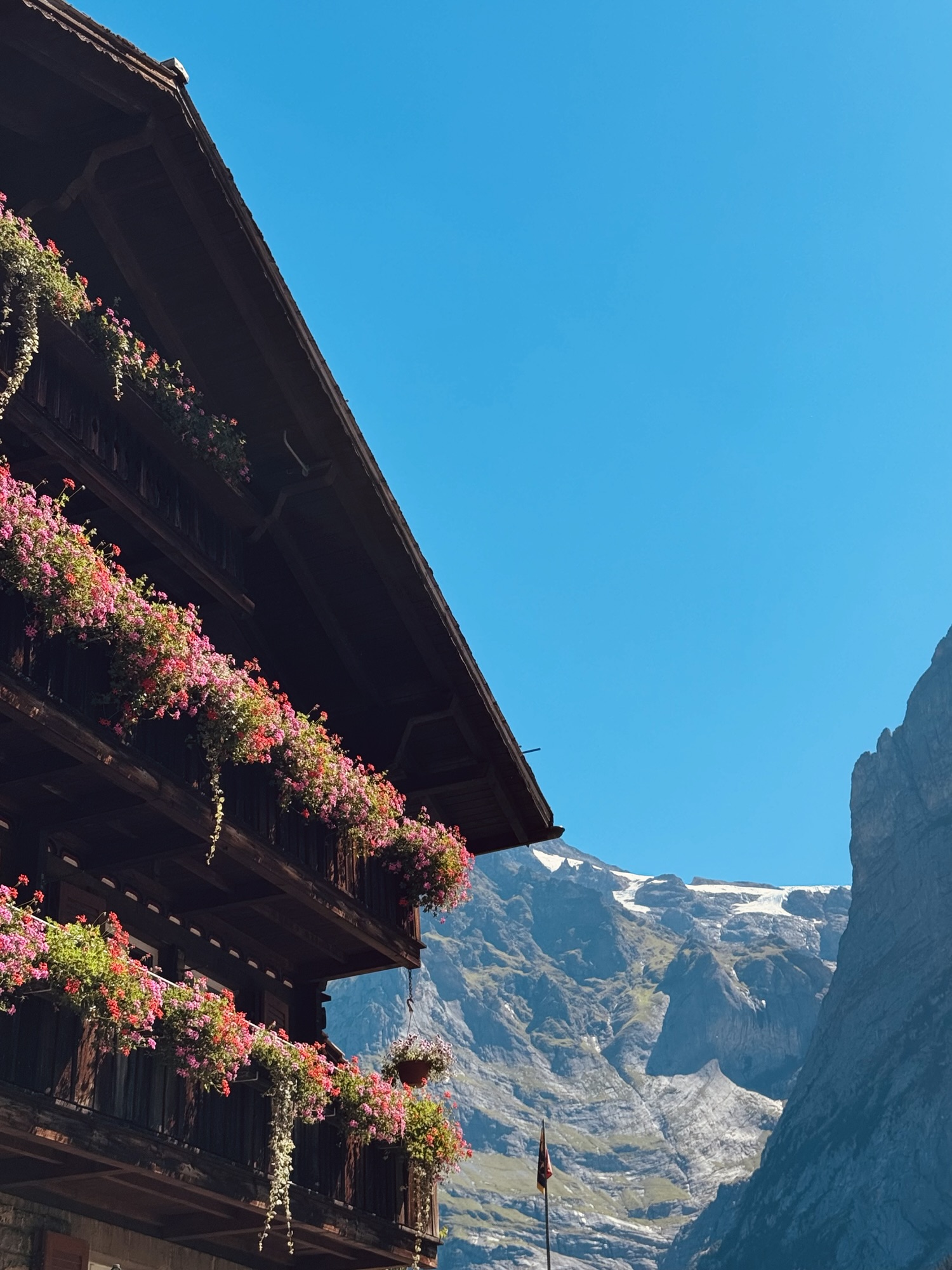 Beautiful Swiss home with colorful flowers hanging from balconies and mountain in the background