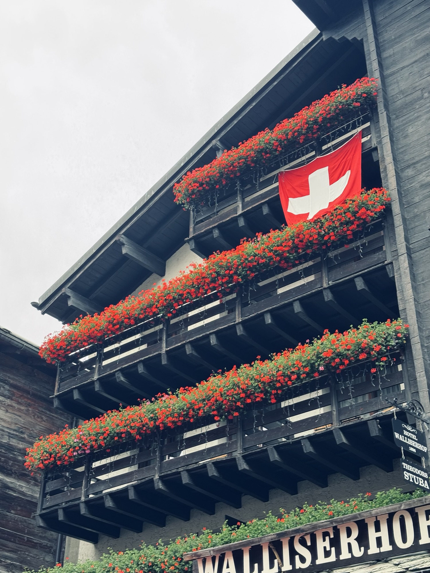 Black building with red florals on the balconies and swiss flag hanging in Zermatt