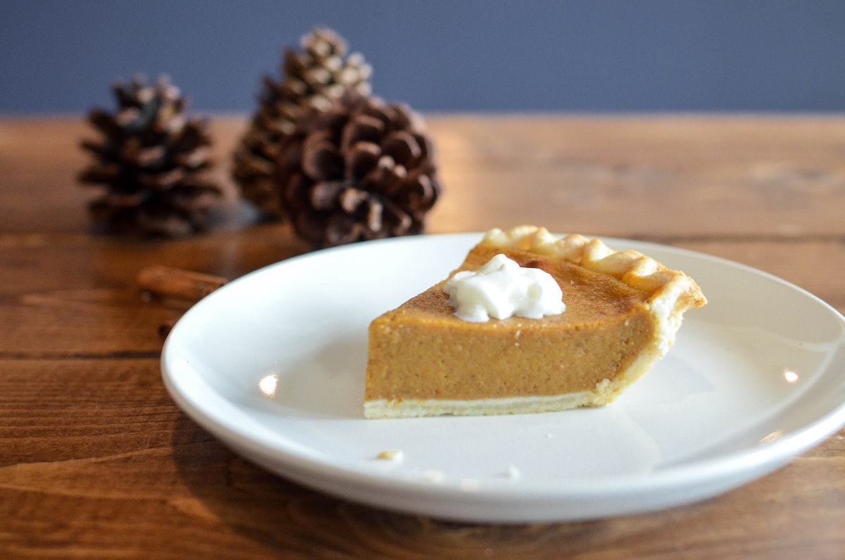 A slice of pumpkin pie on a plate and pinecones in the background